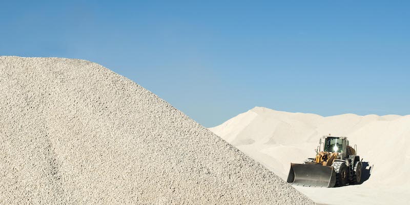 A massive pile of white calcium carbonate dwarfs a bulldozer