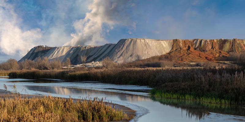 A large mound of phosphogypsum byproduct looms over a riverbank