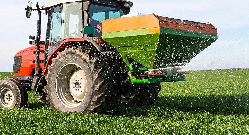 Red tractor spreading solid fertilizer in a field